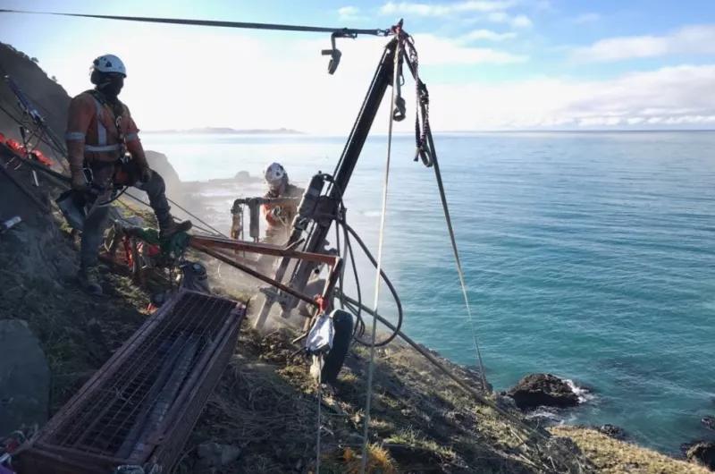 An Avalon geotechnical team with a rigged drill on a slope above the sea