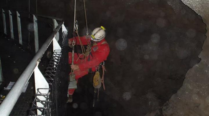 Avalon technician on rope installs safety railing underground