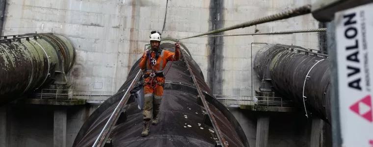 Avalon team member attached to safety cable walking on dam pipeline