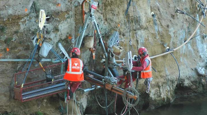 Avalon team members and heavy drill equipment hanging on a rock face