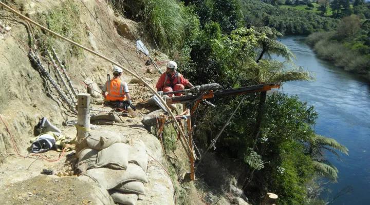 Avalon team members with a drilling rig on a dirt slope above the Waikato river